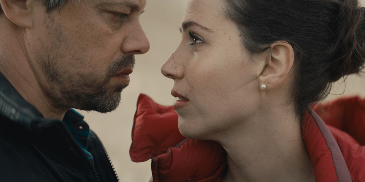 Cena do filme Ahed's Knee mostra o close-up de um homem e uma mulher muito próximos um do outro, se olhando nos olhos.