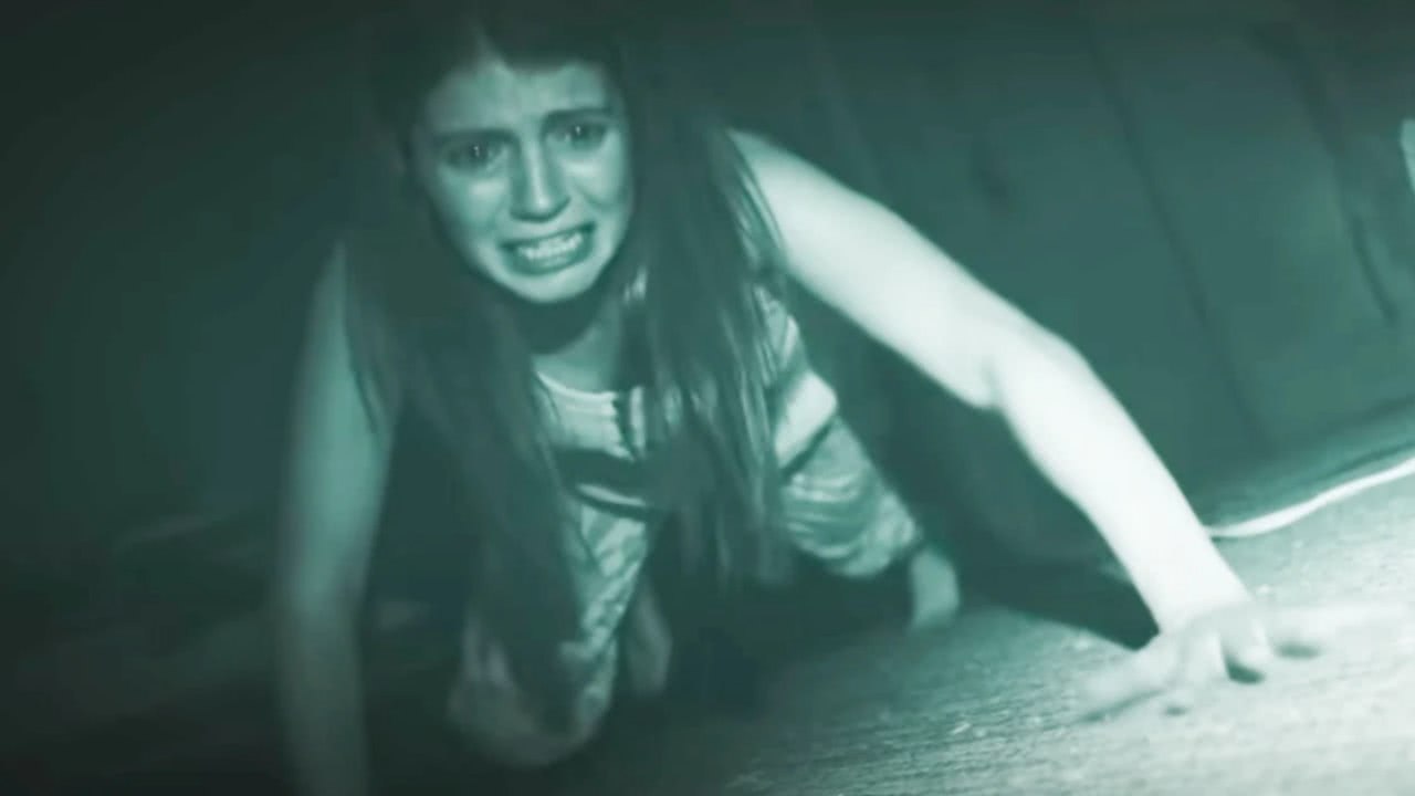 Cena do filme Atividade Paranormal 7, mostra a visão noturna de uma mulher agachada chorando de medo.