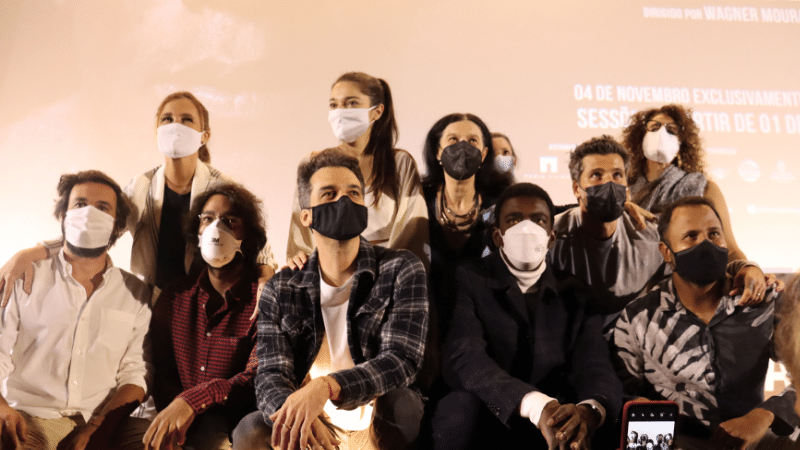 Foto da coletiva de imprensa, mostra os atores, produtores e roteiristas posando para a foto, reunidos e todos de máscara