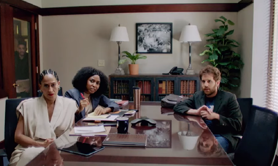 Cena da série The Premise, mostra o interior de uma firma de advogados, com duas mulheres negras atendando um cliente branco. Eles se sentam à mesa marrom e olham para um monitor, com expressões de susto.