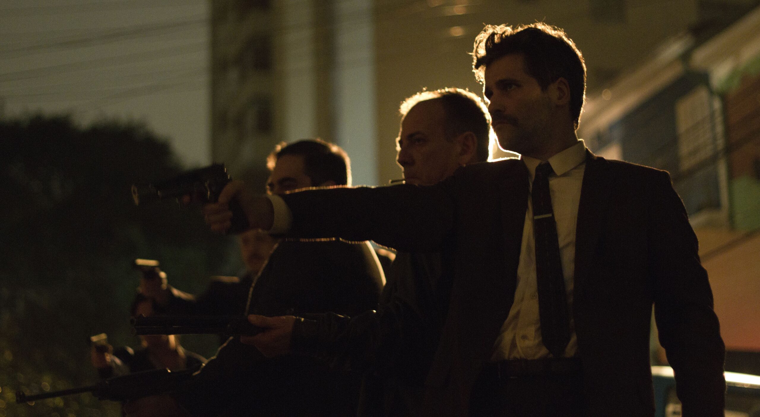 Cena noturna do filme Marighella, mostra vários homens com armas apontadas para um mesmo lugar, atirando.