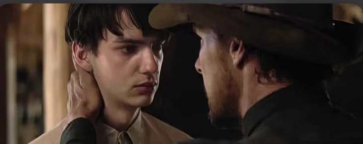 Cena do filme Ataque dos Cães, mostra o jovem Peter olhando para Phil, o caubói de chapéu. Peter é um homem branco, tem cabelos pretos e Phil é mais velho, tem a pele suja e barba. 