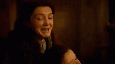 Gif retangular horizontal. Cena da série Game of Thrones. O gif mostra a personagem Catelyn Stark com uma mulher morta em seus braços. Ela grita com expressão de desespero.