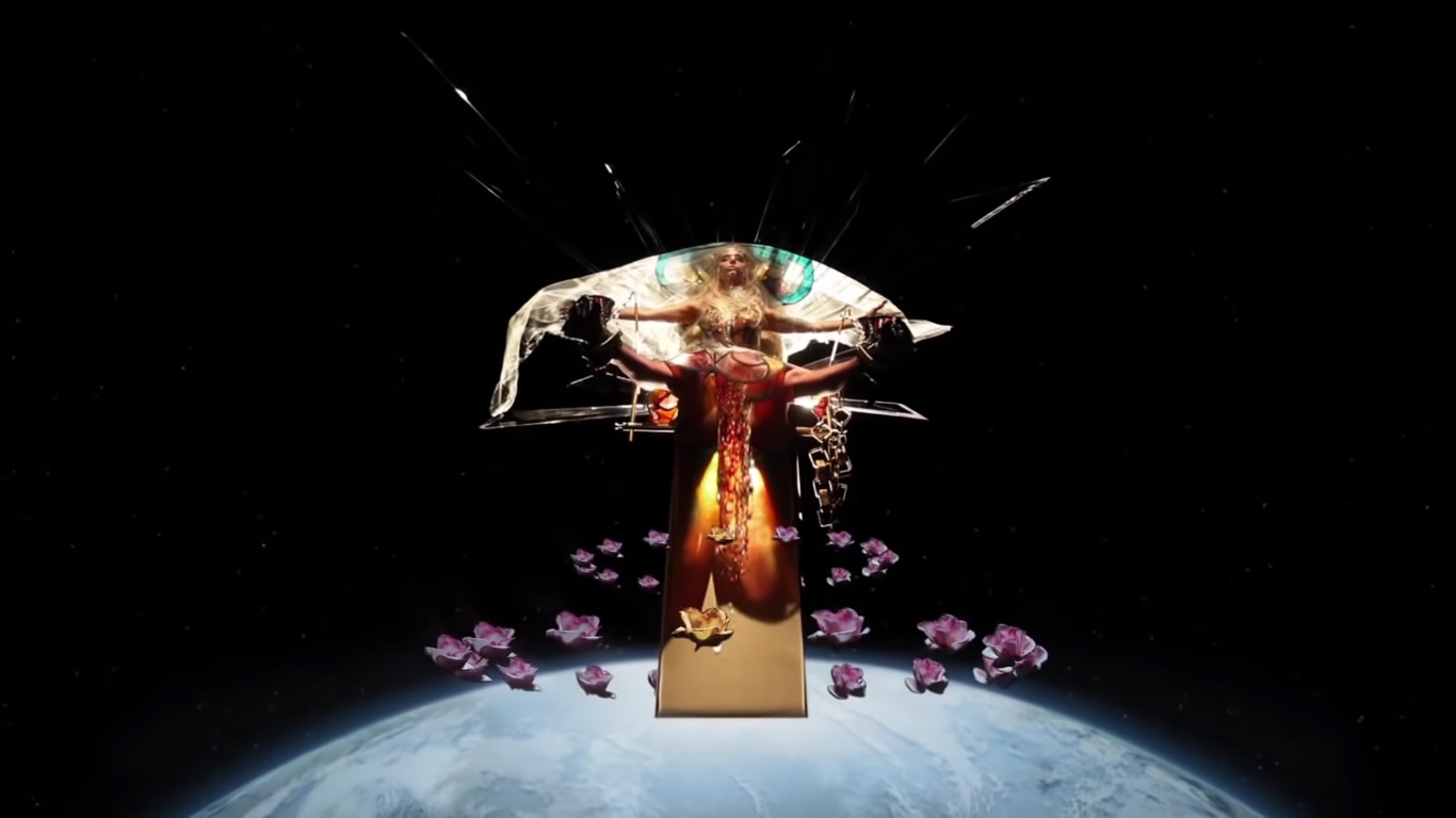 Cena do clipe Born This Way. A imagem mostra a cantora Lady Gaga no espaço acima do planeta Terra. Ela está deitada no que aparenta ser um trono, com as pernas abertas. Rosas rodeiam o objeto.