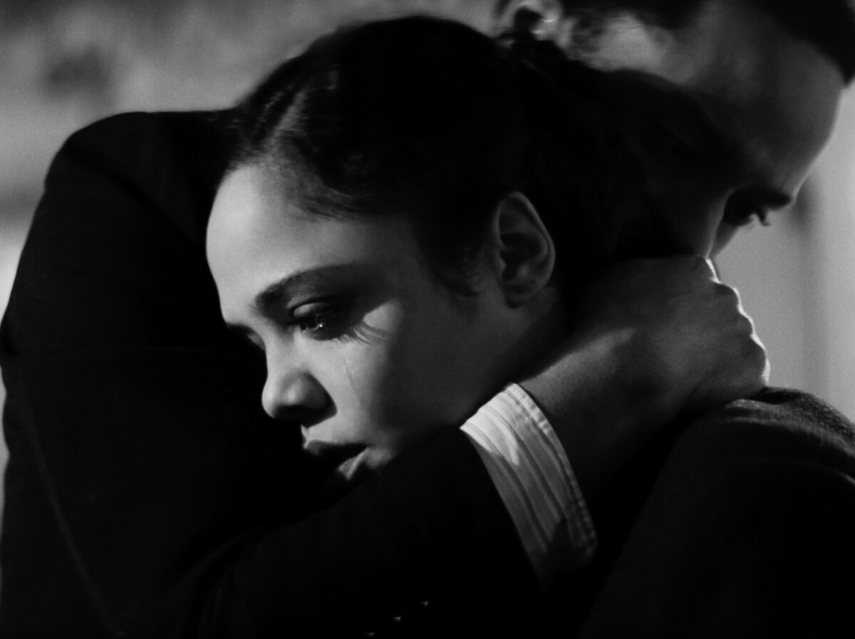 Cena em preto e branco do filme Identidade. Vemos uma mulher sendo abraçada por um homem, ambos são negros. Ela olha para a frente com expressão de choque e tristeza.
