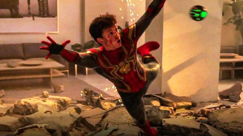 Cena do filme Homem-Aranha: Sem Volta para Casa. A cena mostra o Homem-Aranha, um jovem branco, se jogando para pegar uma bolha laranja e verde. Ele usa o uniforme vermelho, com detalhes em preto e o cenário ao seu redor é de escombros e destruição.