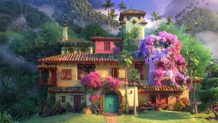 Cena do filme animado Encanto, mostra uma imagem da Casita, a residência dos Madrigal. A casita tem vários andares, é colorida, cheia de flores e folhas e ao seu redor vemos a floresta e as montanhas.