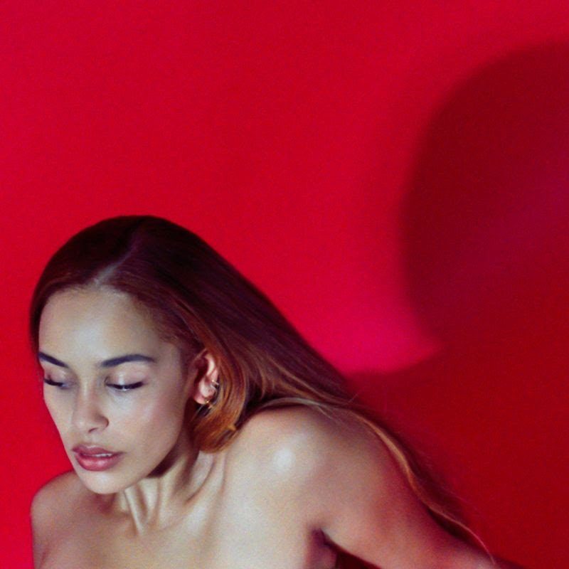 Capa do EP Be Right Back. A imagem mostra Jorja Smith, uma mulher negra e jovem, de cabelos ruivos e longos. Ela é fotografada do busto para cima, mantendo seu olhar direcionado para baixo. Ao fundo, um painel vermelho reflete sua sombra parcialmente.