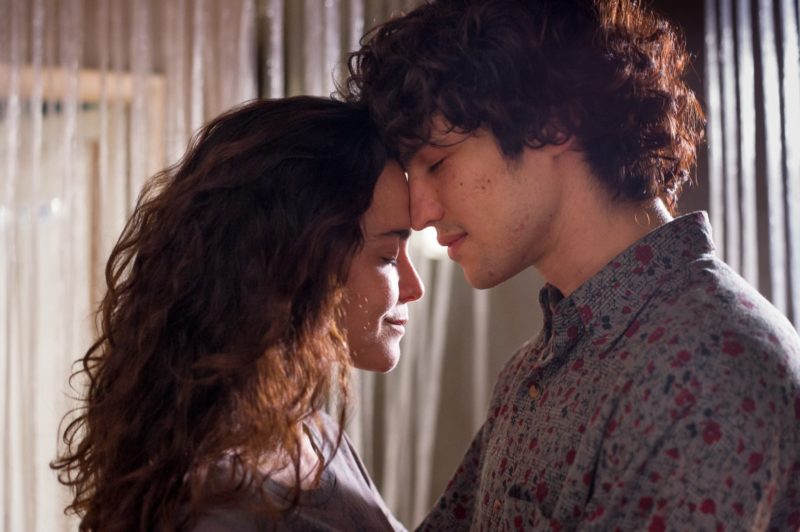 Cena do filme Eduardo e Mônica, em que é mostrado o casal unido, com as testas grudadas uma na outra, prestes a se beijar. Vestem camisetas com tons neutros de roxo.