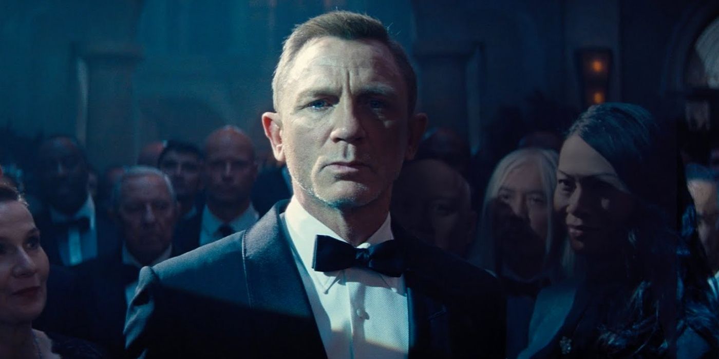 Cena do filme 007 - Sem Tempo para Morrer. Nela, James Bond, personagem de Daniel Craig, aparece em um baile de gala. Centralizado na imagem e aparecendo do tronco para cima, Bond, um homem loiro, olhos claros e meia idade, veste um smoking preto, uma camisa branca e uma gravata borboleta preta. Atrás de Bond, seis pessoas o rodeiam, quatro homens e duas mulheres, todos também vestidos para um evento de gala. Na cena, um holofote está voltado para Bond, onde seu lado direito está iluminado e o lado esquerdo não, de forma a criar um contraste.