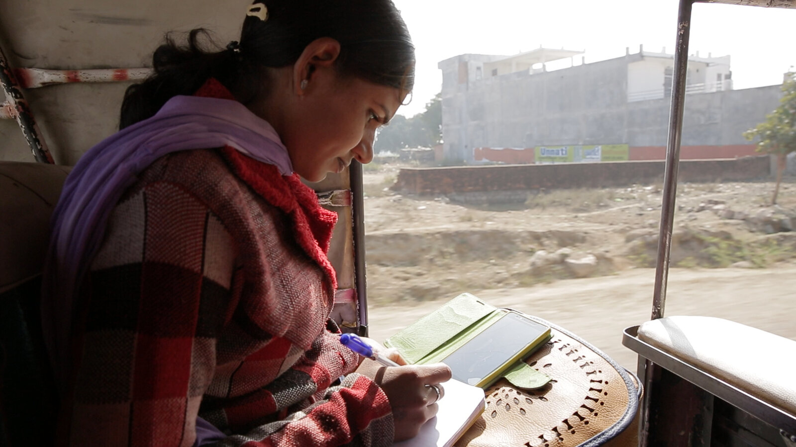 Cena do documentário Escrevendo com Fogo. A cena mostra uma mulher debruçada sobre um caderno, olhando a tela de um celular e anotando algo no papel.
