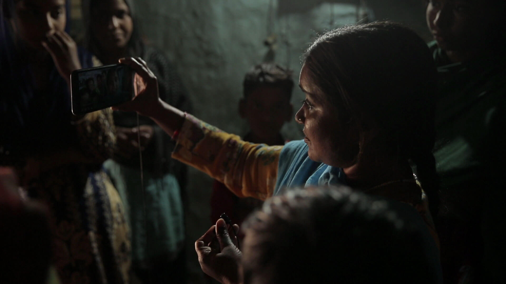 Cena do documentário Escrevendo com Fogo. A cena mostra uma mulher filmando com o celular em um ambiente escuro e cheio de outras pessoas ao redor.