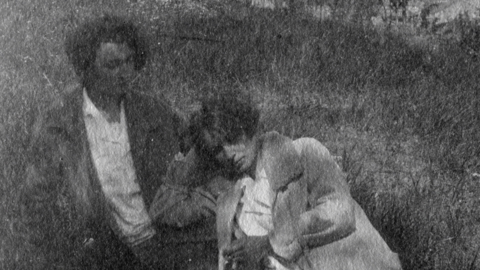 Cena do filme Ultravioleta e a Gangue das Cuspidoras de Sangue, que mostra uma fotografia granulada em preto e branco de duas garotas. Uma permanece sentada e a outra se escora no corpo da outra menina, apoiando a cabeça com as mão direita.