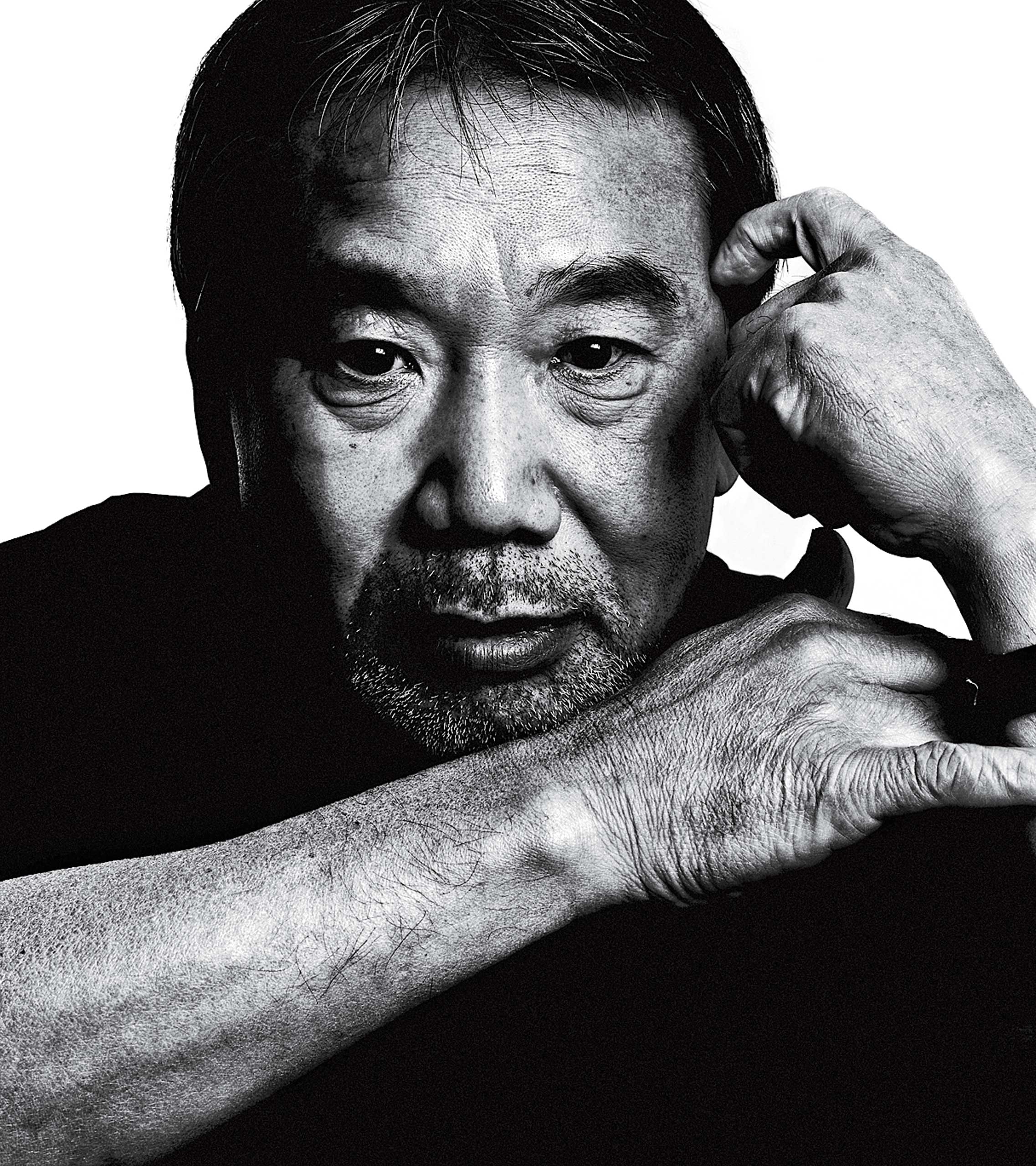 Foto em preto e branco do escritor japonês Haruki Murakami. Ele é um homem com traços asiáticos, possui cabelo e barba grisalhos, e na foto está olhando diretamente para a câmera, com a mão esquerda sobre a têmpora esquerda e seu braço direito apoiado sobre o braço esquerdo. O fundo da imagem é branco. 