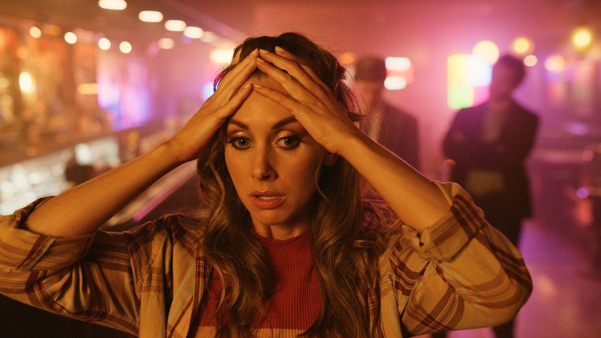 Cena da série Roar, mostra uma mulher branca assustada em uma boate com luzes roxas. Ela tem as mãos na testa, com expressão de surpresa. 