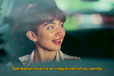 Cena do filme Crush. O GIF tem formato retangular, e mostra Paige falando sobre músicas enquanto está no banco do passageiro do carro. 