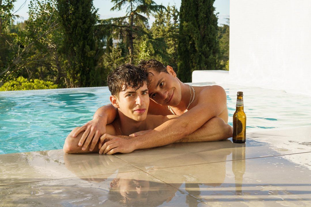 Cena da série Elite mostra dois jovens brancos e magros abraçados à beira da piscina, com um garrafa de cerveja ao lado.