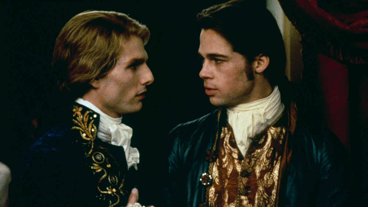 Cena do filme Entrevista com o Vampiro, mostra dois homens brancos se olhando. Um deles, à esquerda, é loiro, e o outro é moreno, eles usam roupas antigas, com detalhes em azul e dourado e tem a pele branca de vampiro.