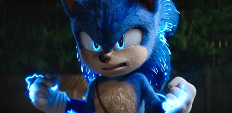 Cena do filme Sonic 2. Sonic está olhando para frente, com uma expressão de raiva. Ele está com as mãos fechadas em punhos, com pequenos raios de energia saindo de suas mãos e espinhos. O ouriço está posicionado em um quintal com árvores e uma cerca, durante a noite.
