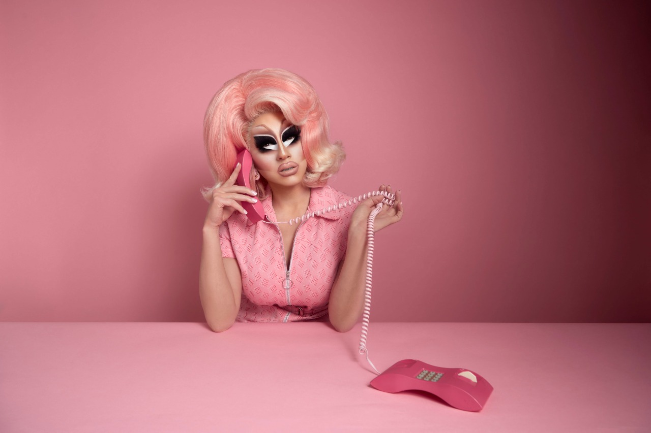 Foto de divulgação do The Pink & Blonde Albums. Na imagem a drag queen Trixie Mattel aparece em um cenário todo rosa segurando um telefone com fio na mesma cor, a artista ainda usa uma roupa e uma peruca seguindo o leque de tons rosa.