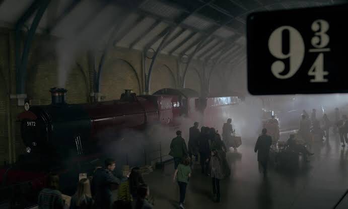 Cena do documentário Harry Potter 20th Anniversary: Return To Hogwarts apresenta um trem ao fundo coberto com fumaça liberada pela própria locomotiva. A sua frente há várias pessoas circulando pela estação. No canto superior direito há em destaque uma placa com o número 9 ¾.