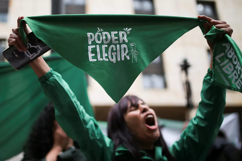Fotografia de um protesto pela legalização do aborto na Colômbia. A imagem mostra uma mulher em segundo plano segurando uma bandeira verde, que em espanhol, diz “poder decidir”