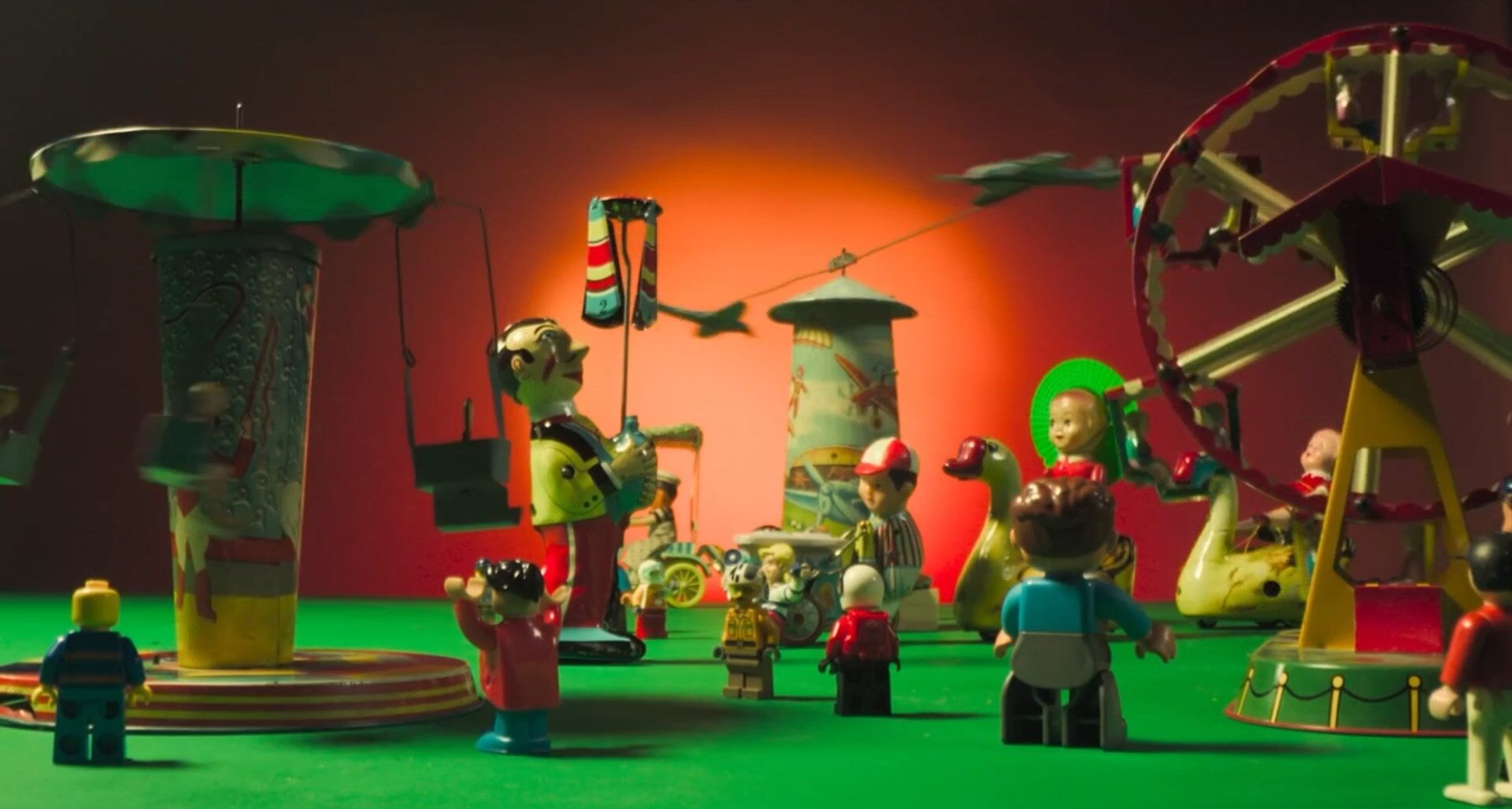 Cena do filme Cinema Almanac. Nela, vemos vários brinquedos em cima de uma superfície verde, em um ambiente com fundo vermelho que parece um parque de diversões, com roda gigante, chapéu mexicano e um trenzinho. Os bonecos que estão no cenário variam de tamanho, alguns pequenos e outros bem maiores. 