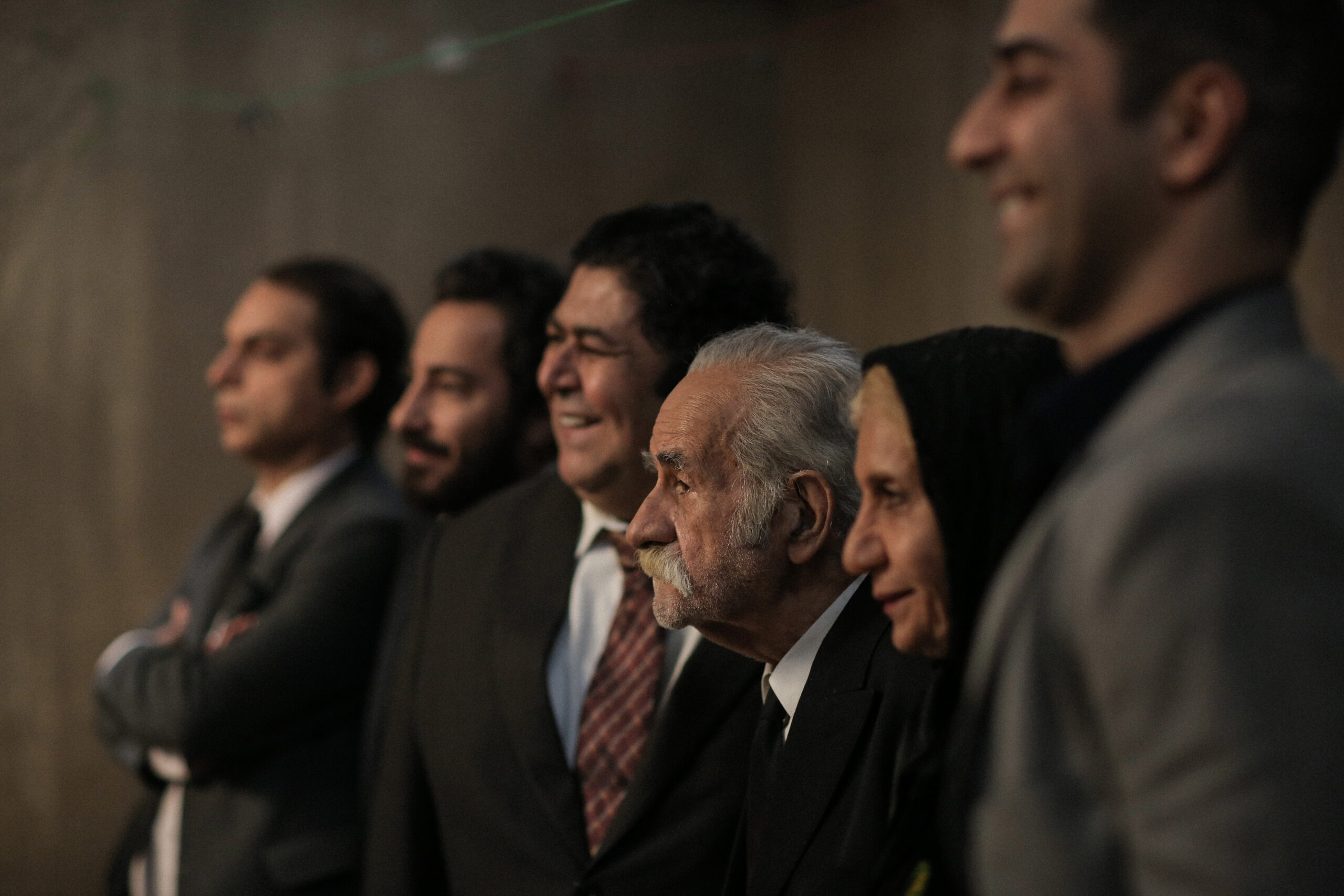 Cena do filme Os Irmãos de Leila, mostra seis pessoas enfileiradas, sorrindo e olhando para a frente. A imagem mostra uma visão lateral das pessoas, que posam para a foto, lado a lado. 