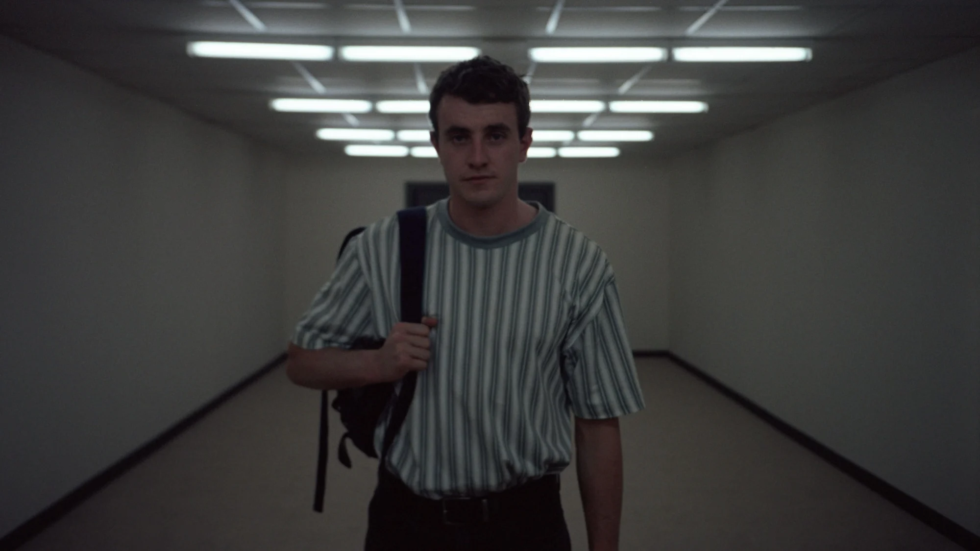 Cena do filme Aftersun, mostra o pai sozinho em um corredor vazio, segurando uma alça da mochila no ombro e olhando para a câmera.