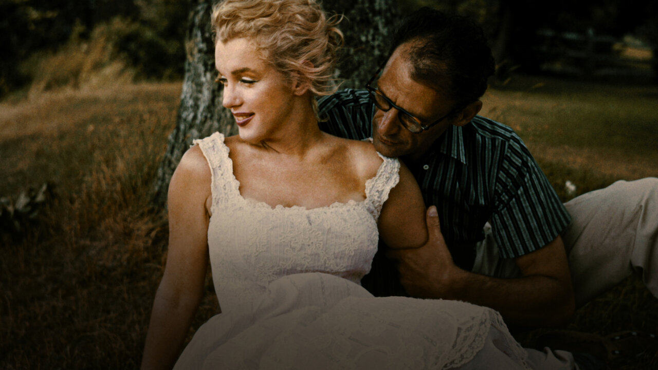 Fotografia presente no filme "O Mistério de Marilyn Monroe". Uma mulher loira olha sorridente para o horizonte. Um homem de óculos de armações escuras pega em seu braço. Ele coloca a cabeça sob seu ombro e olha em direção ao vestido dela. Estão numa paisagem campestre sentados sob uma árvore.
