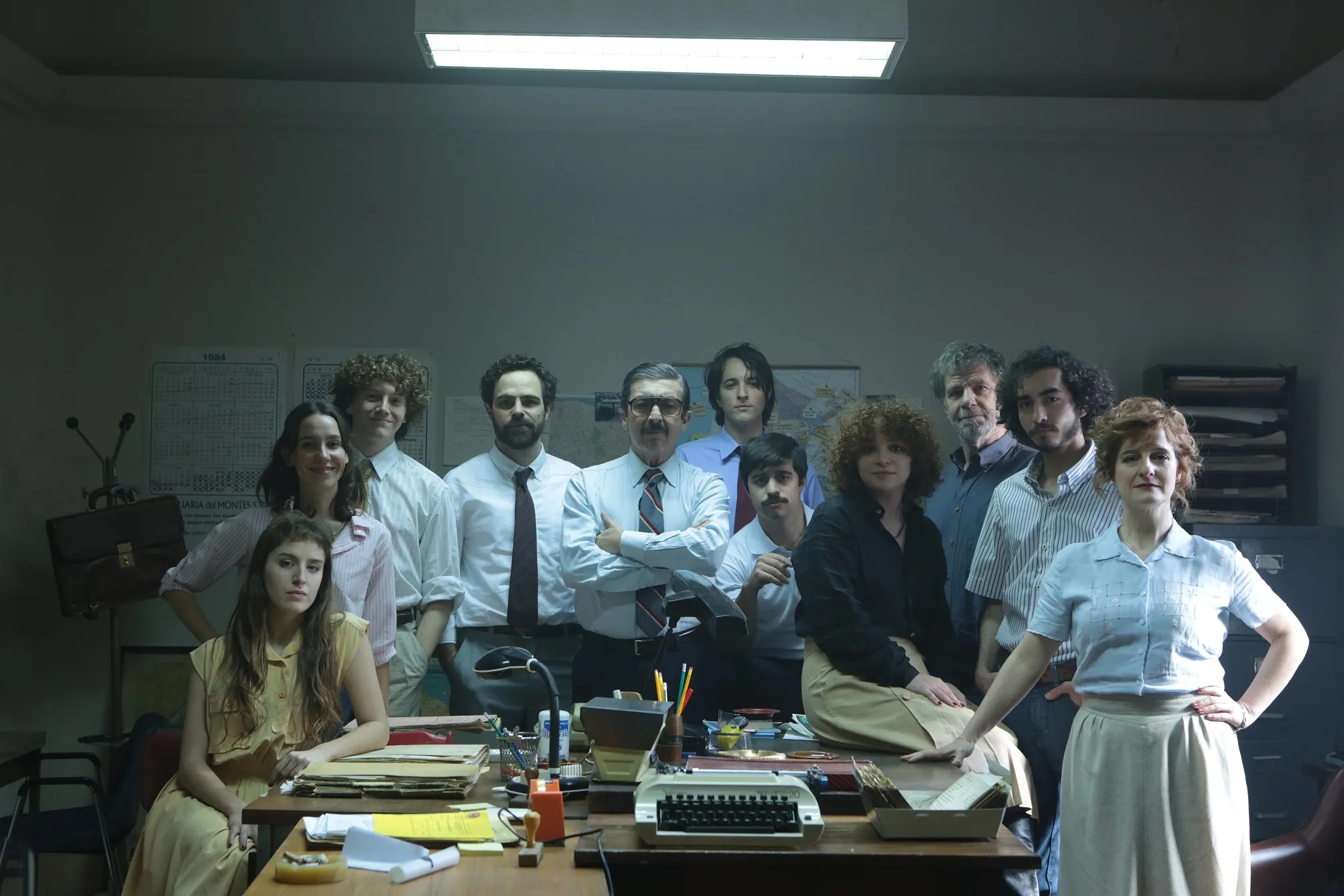 Imagem retangular horizontal do filme Argentina, 1985. A imagem mostra um grupo de pessoas posicionado ao redor de uma mesa em um escritório. São onze pessoas, todas latinas, quatro delas são mulheres, apenas três são mais velhos.
