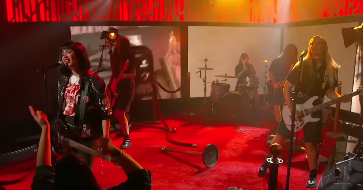 Foto da apresentação de Demi Lovato e sua banda no programa de TV Jimmy Kimmel Live. A imagem tem formato retangular e exibe Demi e as outras quatro mulheres de sua banda enquanto se apresentam.