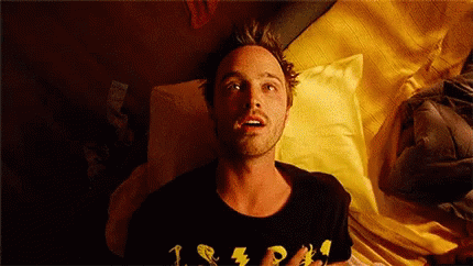  Gif de cena em que o personagem Jesse Pinkman utiliza heroina e “flutua” em sua cama. Jesse é um homem branco de cabelos loiros, veste uma blusa preta com detalhes amarelos. O fundo é a sua cama com travesseiro e lençol.