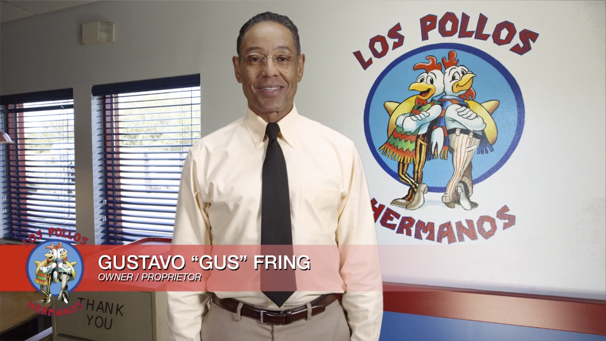 Foto com o fundo em um restaurante escrito “Los Pollos Hermanos” com a logomarca de dois galos mexicanos. Ao centro, o personagem Gus Fring olha para a câmera. Ele é um homem negro, veste camisa branca, oculos, gravata preta e calça bege de alfaiataria.