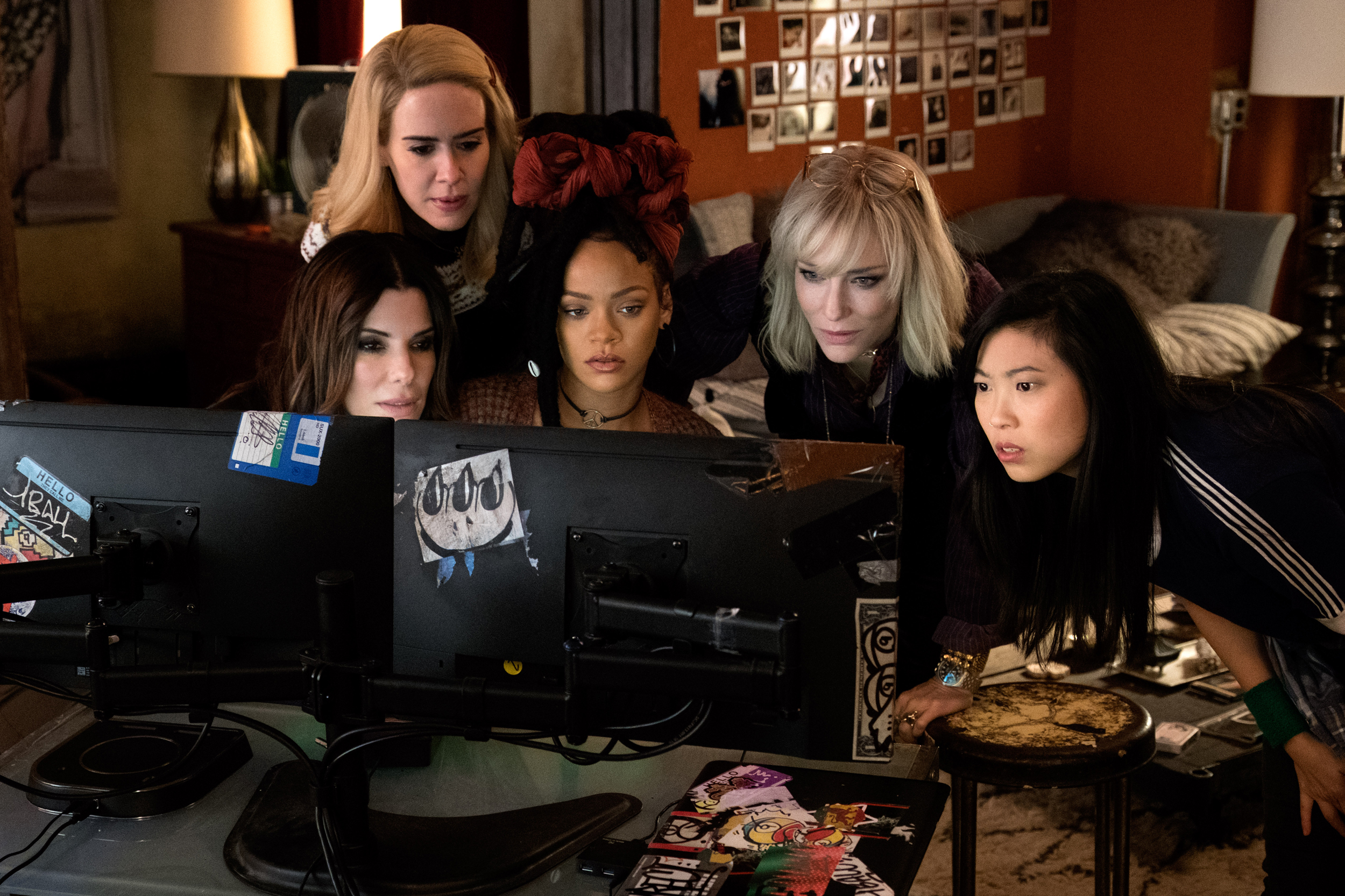 Cena do filme Oito Mulheres e um Segredo. Da esquerda para direita, Sandra Bullock, Sarah Paulson, Rihanna, Cate Blanchett e Awkwafina olhando para a tela de um computador. 