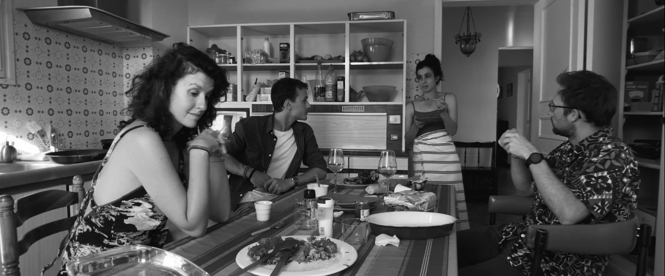Cena do filme La Parle. A imagem é em preto e branco. Em uma cozinha, aparecerem, esquerda para a direita: Fanny Boldini, Simon Boulier, Kevin Vanstaen e Gabriela Boeri