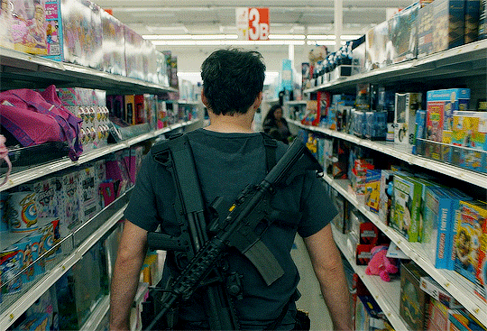 Cena da série Barry. A imagem mostra as costas de Barry, que está carregando duas armas apoiadas em seus ombros, enquanto ele anda entre corredores de uma loja cheios de brinquedos infantis.