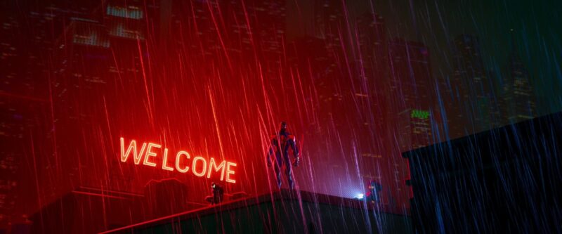 Cena do filme Homem-Aranha: Através do Aranhaverso. A cena mostra Miguel O’hara, o Homem-Aranha 2099, em pé em cima de um prédio, no centro da imagem. Sua silhueta está tampada pela chuva, e, atrás dele há um letreiro em vermelho neon escrito “Welcome”.