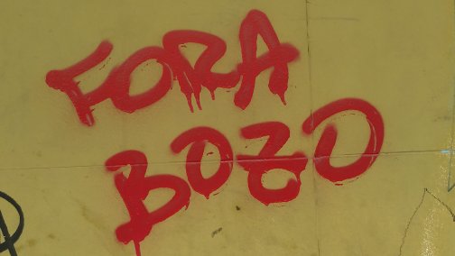 Cena do documentário Pele, de 2021. A imagem contém uma parede amarela, com os escritos “FORA BOZO” grafitados em caixa alta, na cor vermelha.