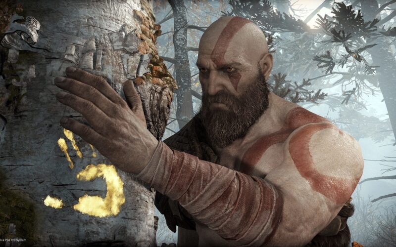 Há apenas uma figura na imagem, que é Kratos, à direita, colocando a mão em uma árvore branca à esquerda. É possível ver que a árvore está marcada com um símbolo dourado e brilhante da palma de uma mão. O braço de Kratos está em primeiro plano e nele se destacam bandagens sujas que cobrem as cicatrizes do protagonista. 