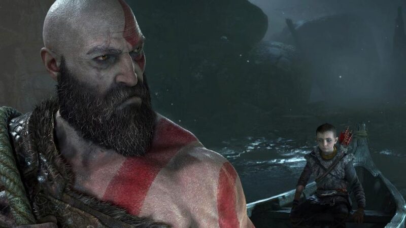Tem duas pessoas na imagem. Na esquerda está Kratos, ele aparece do peito para cima e olha por cima do ombro para Atreus, que está à direita da imagem, ele veste uma camiseta cinza de manga comprida e um colete de pele por cima. Eles estão em um barco. O fundo da imagem é cinza.