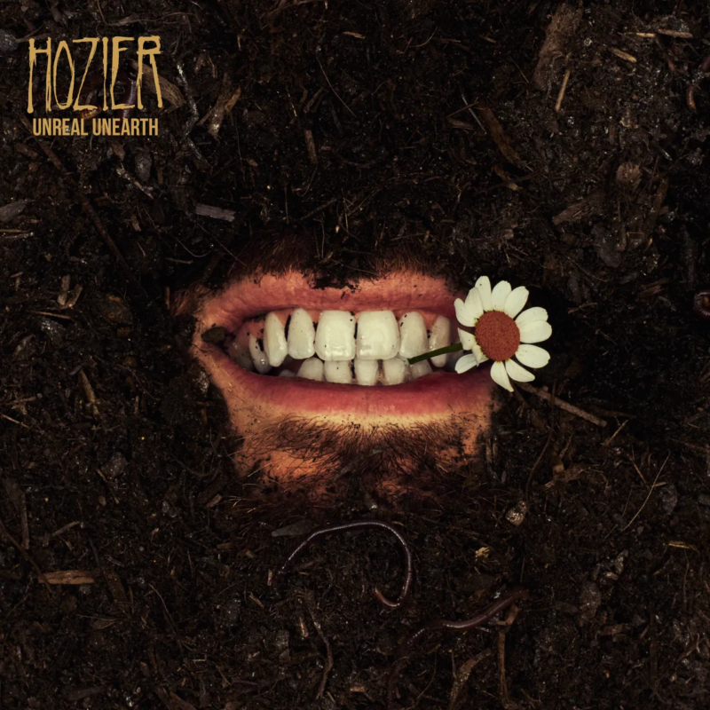 Capa do álbum Unreal Unearth, de Hozier. Nela vemos uma boca masculina emergindo da terra, ela está segurando uma margarida com os dentes. No cantio superior esquerdo, em letras estilizadas está escrito "Hoziier" e logo abaixo, "Unreal Unearth".