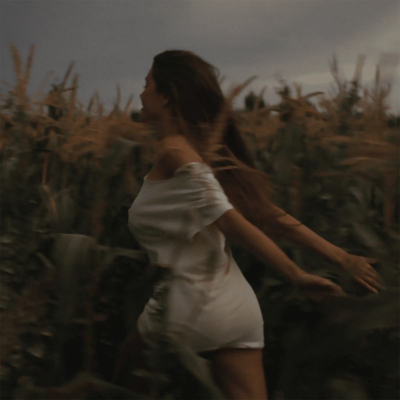 Capa do disco Silence Between Songs, da cantora estadunidense Madison Beer. A imagem mostra a artista correndo por uma plantação, em um dia nublado. Madison é uma mulher branca, de cabelos castanhos, que usa um vestido branco curto.