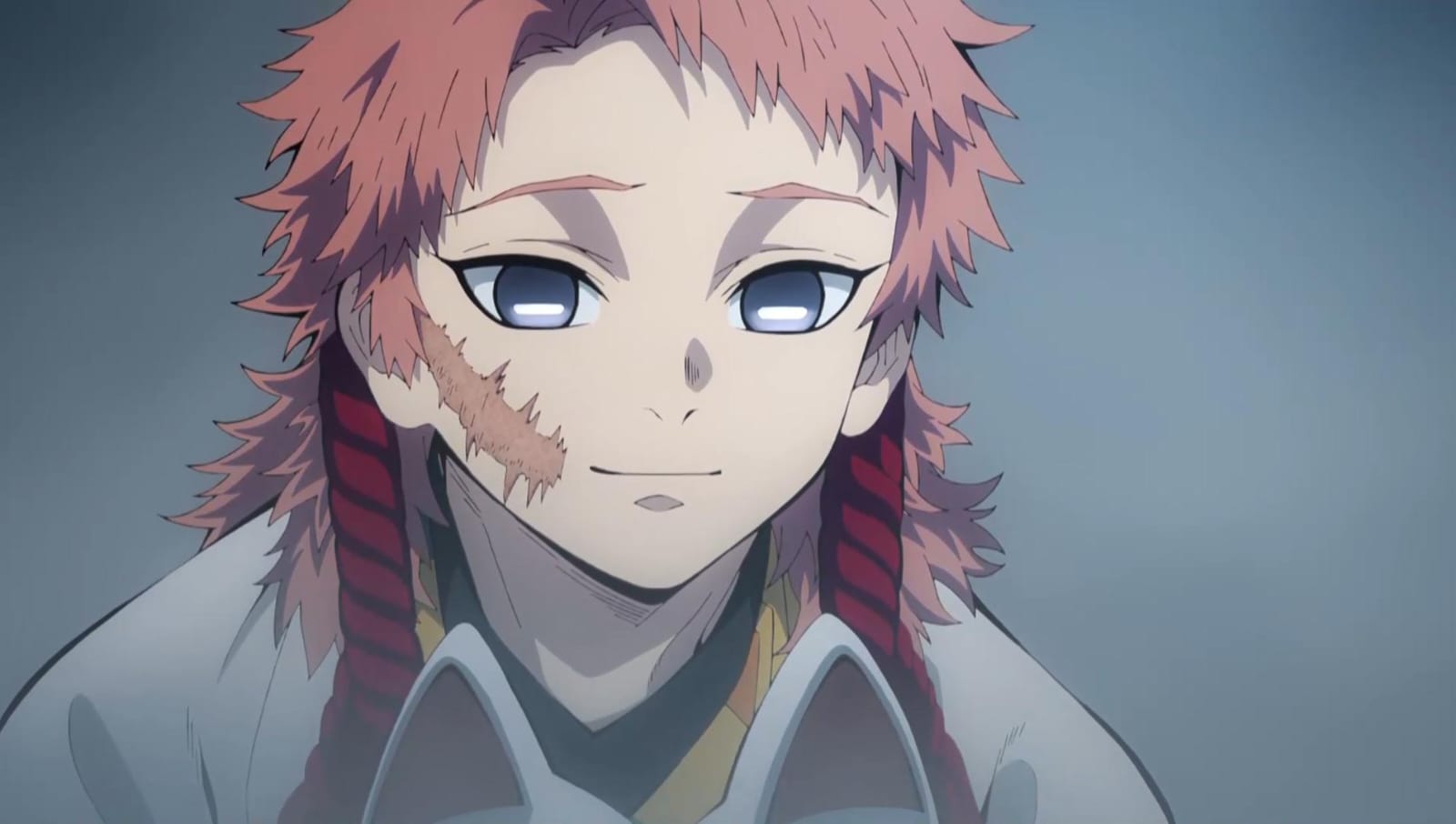 Na imagem um cena do anime Demon Slayer; na imagem temos Sabito, ele é um jovem branco, japonês, de cabelo ruivo cobre claro, sobrancelhas finas da mesma cor, olhos grandes e tristes de cor cinza, nariz pequeno, boca fina e queixo pontiagudo; Sabito tem uma cicatriz grande na bochecha esquerda, ele veste um conjunto de kimonos verde ao fundo, amarelo por cima e por fim branco, ao redor de seu pescoço carrega uma corda vermelha e grossa, que anteriormente mantinha uma máscara presa a seu rosto.