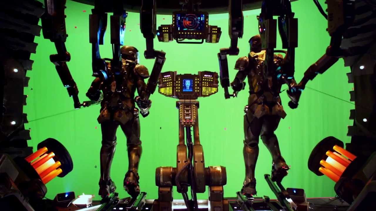 Gravação de uma cena dentro de um Jaeger em Círculo de Fogo (2013). Em frente a uma tela verde está construído um cenário que simula o ambiente dentro de um robô gigante, enquadrando a foto com engrenagens e pistões vermelho-brilhantes simetricamente em ambos os lados. Ao centro está o painel de controle, e duas pessoas ao seu lado em pé, porém conectadas nos braços, pernas e capacetes ao resto da maquinaria. Suas armaduras e equipamentos são cinzentos, e os botões no painel de controle são amarelos e contam com duas telas azuis.