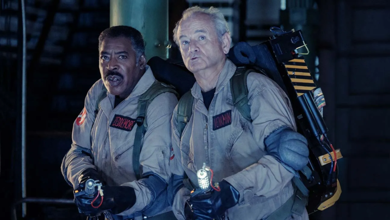 Cena do filme Ghostbusters: Apocalipse de Gelo. Peter Venkman e Winston Zeddemore com suas ferramentas equipadas. O primeiro é um homem negro, com cabelo e bigode preto. O segundo é um homem idoso branco. Ambos estão usando os famosos uniformes dos caça-fantasmas.