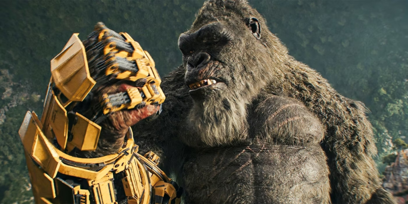 Cena do filme Godzilla e Kong: O novo Império. A imagem foca no gorila gigante Kong, que está cheio de machucados. Ele olha com curiosidade para uma luva robótica amarela em sua mão. Ao fundo,tem uma floresta bem distante.