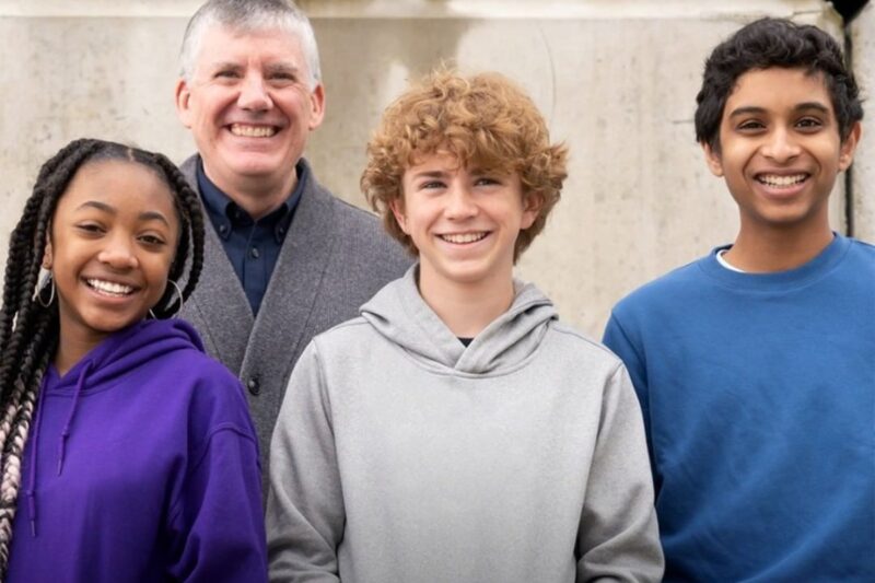 Foto do elenco de Percy Jackson e os Olimpianos. Nela, vemos, da esquerda para direita: Leah Sava Jeffries, uma adolescente negra de cabelo trançado. Ela veste um moletom roxo. Walker Scobbel, um adolescente branco de cabelos loiros cacheados. Ele veste um moletom cinza e Aryan Simhadri, um jovem indiano de cabelos pretos e que veste um moletom azul. Atrás deles está o autor Rick Riordan, um homem branco de cabelos brancos. Ele veste um sueter cinza. Ao fundo, uma parede na cor creme.