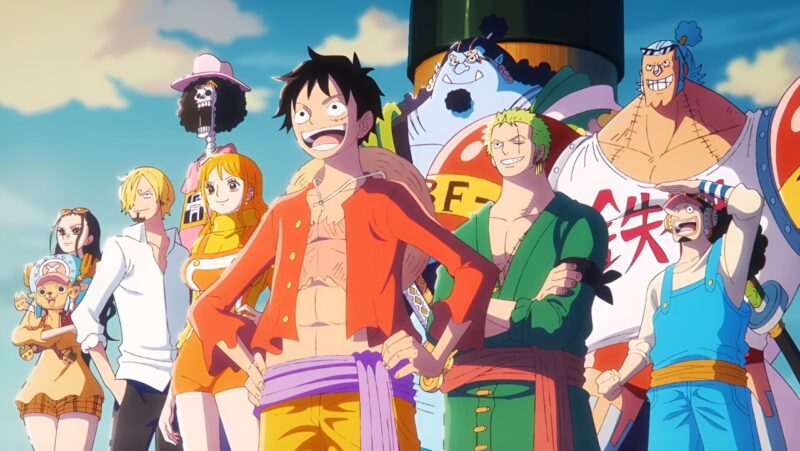 Cena do anime One Piece. Tem dez pessoas na imagem. Da esquerda para a direita está Robin, ela veste uma camiseta marrom e um shorts laranja, em sua cabeça tem um óculos de sol. Nos braços ela segura Chopper, ele usa uma jaqueta vermelha, um shorts vermelho e um chapéu azul com um X no meio. Ao lado aparece Sanji, ele veste uma camisa branca e uma calça preta, e Nami, que usa uma camiseta amarela e uma jardineira laranja. Atrás deles está Brook, ele veste uma camiseta rosa e um chapéu rosa. No centro da imagem está Luffy, ele veste uma camisa vermelha aberta, uma faixa roxa na cintura, uma bermuda amarela e seu chapéu de palha está pendurado nas costas. Do seu lado está Zoro, ele veste um quimono verde e uma faixa vermelha na cintura. Atrás dos dois estão Jinbe, que veste um quimono verde, e Franky, um ciborgue de meia idade branco, ele tem o cabelo azul preso em coque e olhos castanhos, ele veste uma regata branca e uma sunga vermelha, cada um dos seus ombros tem uma bola vermelha grande. Na direita da imagem está Usopp, ele veste uma camiseta bege, uma jardineira azul e um boné vermelho. Eles estão olhando o horizonte e todos estão no navio, então no fundo aparece o mastro e o ceú.