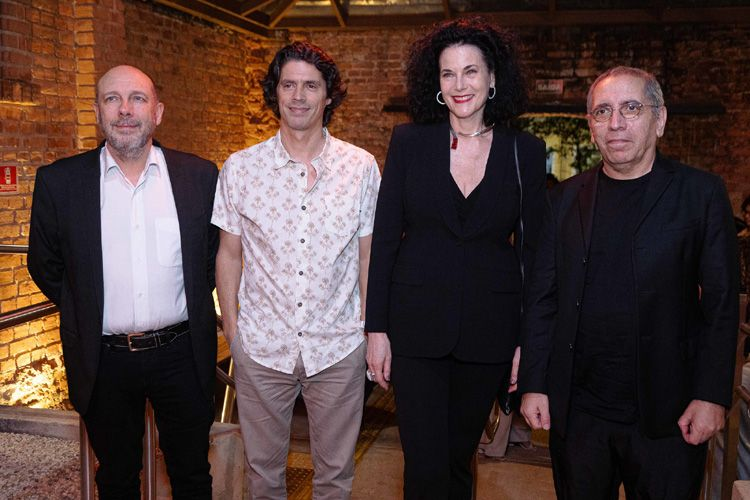 Foto dos jurados da 48ª Mostra Internacional de Cinema de São Paulo: Thierry Méranger, Gonçalo Waddington, Hebe Tabachnik e Mohsen Makhmalbaf. Thierry Méranger, à esquerda, é um homem de meia-idade, com barba e cabelo ralo, vestindo um terno preto e camisa branca, sem gravata. Ao lado dele, Gonçalo Waddington, de cabelos cacheados e volumosos, veste uma camisa clara com estampa discreta. Hebe Tabachnik, terceira da esquerda para a direita, é uma mulher de cabelos escuros, volumosos e cacheados; ela veste um terno preto e usa brincos grandes e um colar. À direita está Mohsen Makhmalbaf, um homem mais velho, de rosto sério e cabelo curto, sem barba, usando um terno preto e camisa preta. Eles estão posicionados em frente a uma parede de tijolos, alinhados lado a lado.